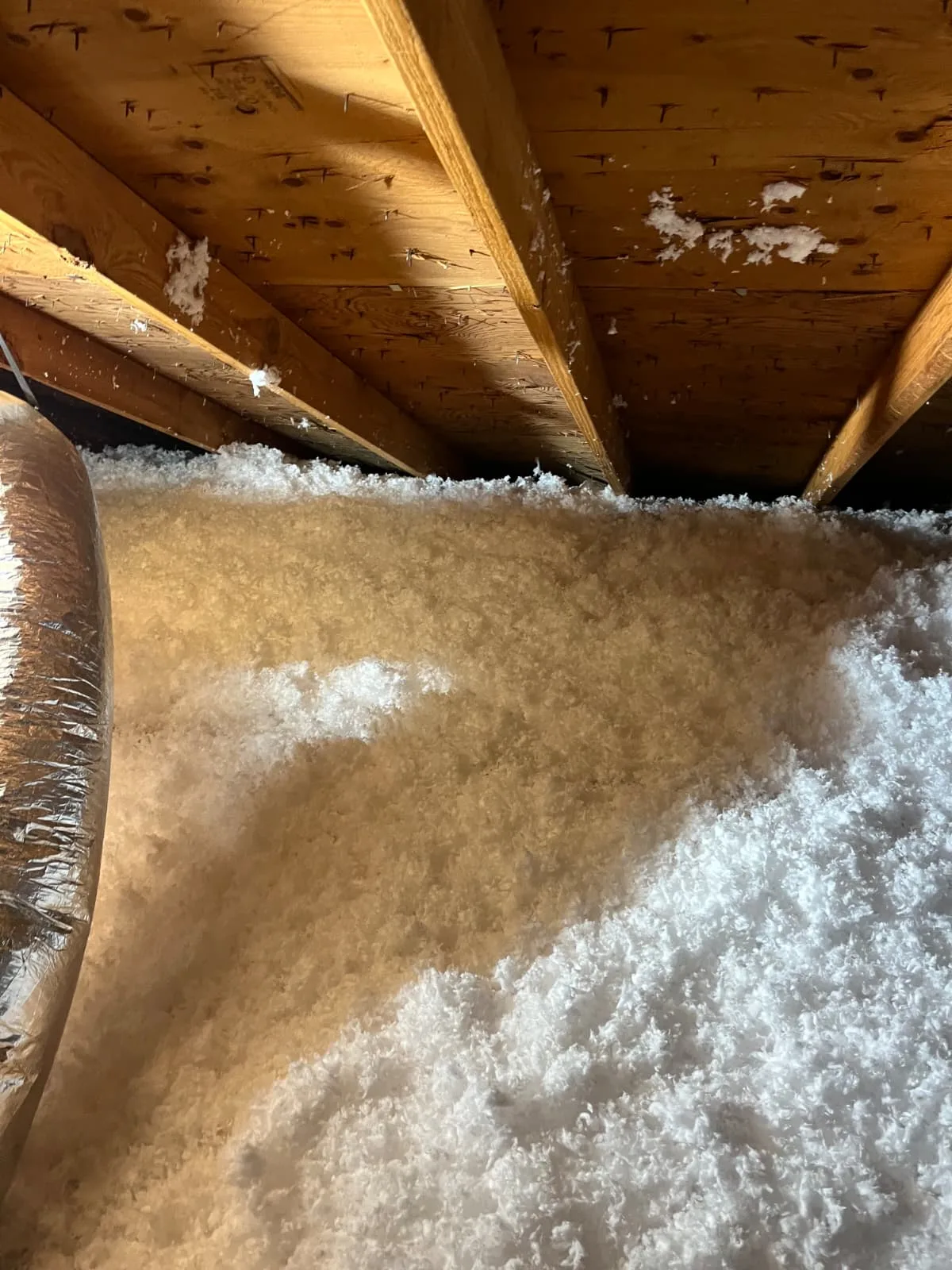 Attic ductwork surrounded by blown-in insulation for even coverage in Greater Houston